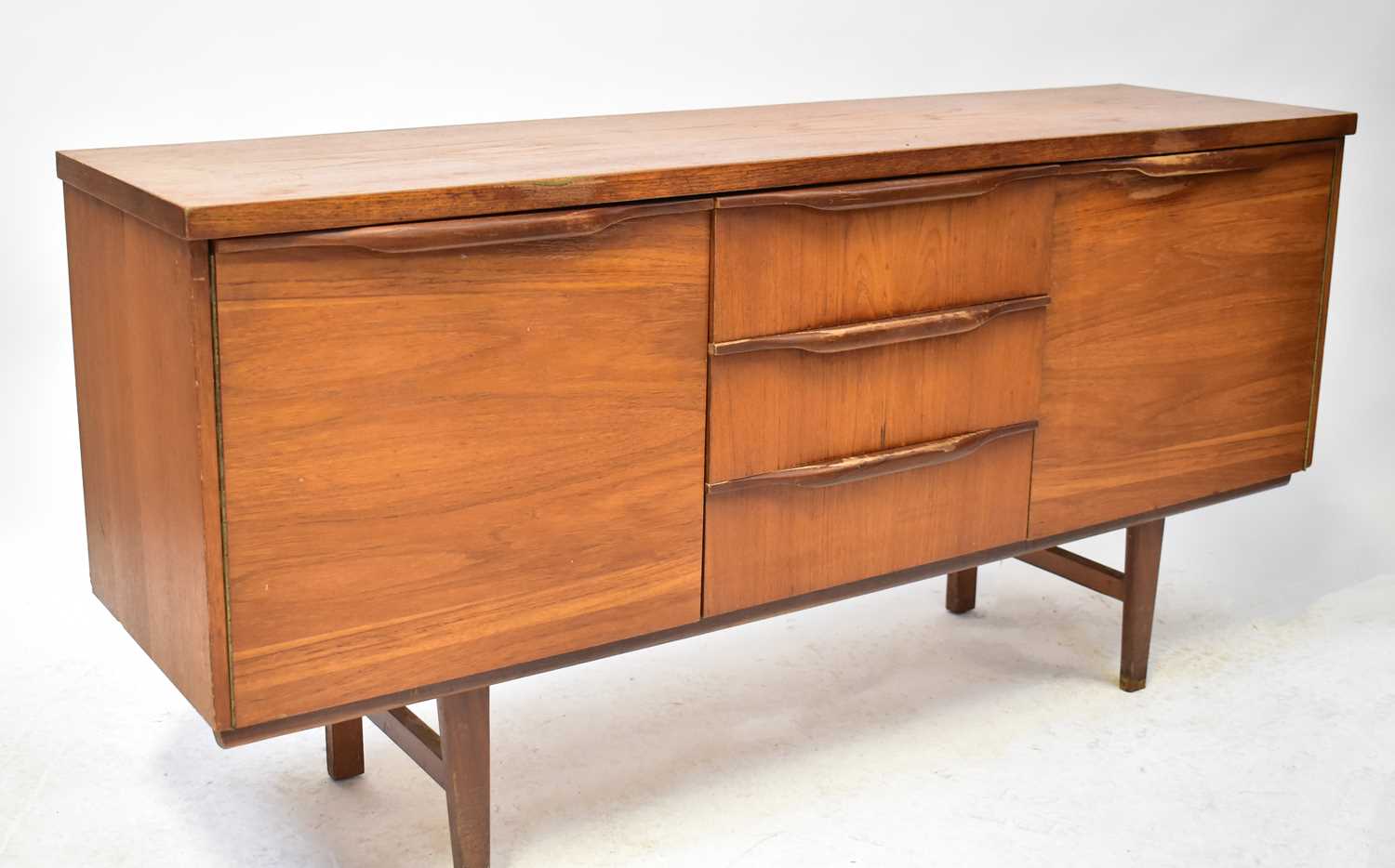A mid-20th century teak sideboard with three short drawers and a pair of cupboard doors, on square