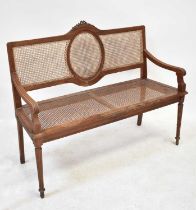 An early 20th century bergère caned two-seater settee, raised on reeded tapering supports to peg