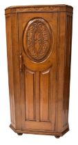 An early 20th century oak hall robe with canted front, single door with carved oval panel, raised on
