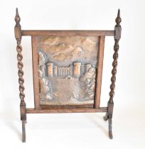 A bronzed and oak fire screen with repoussé bronzed panel of castle with moat, twist side supports