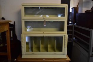 A painted three tier bookcase with glazed up-and-over doors, width 92cm, depth 37cm, height 103cm.