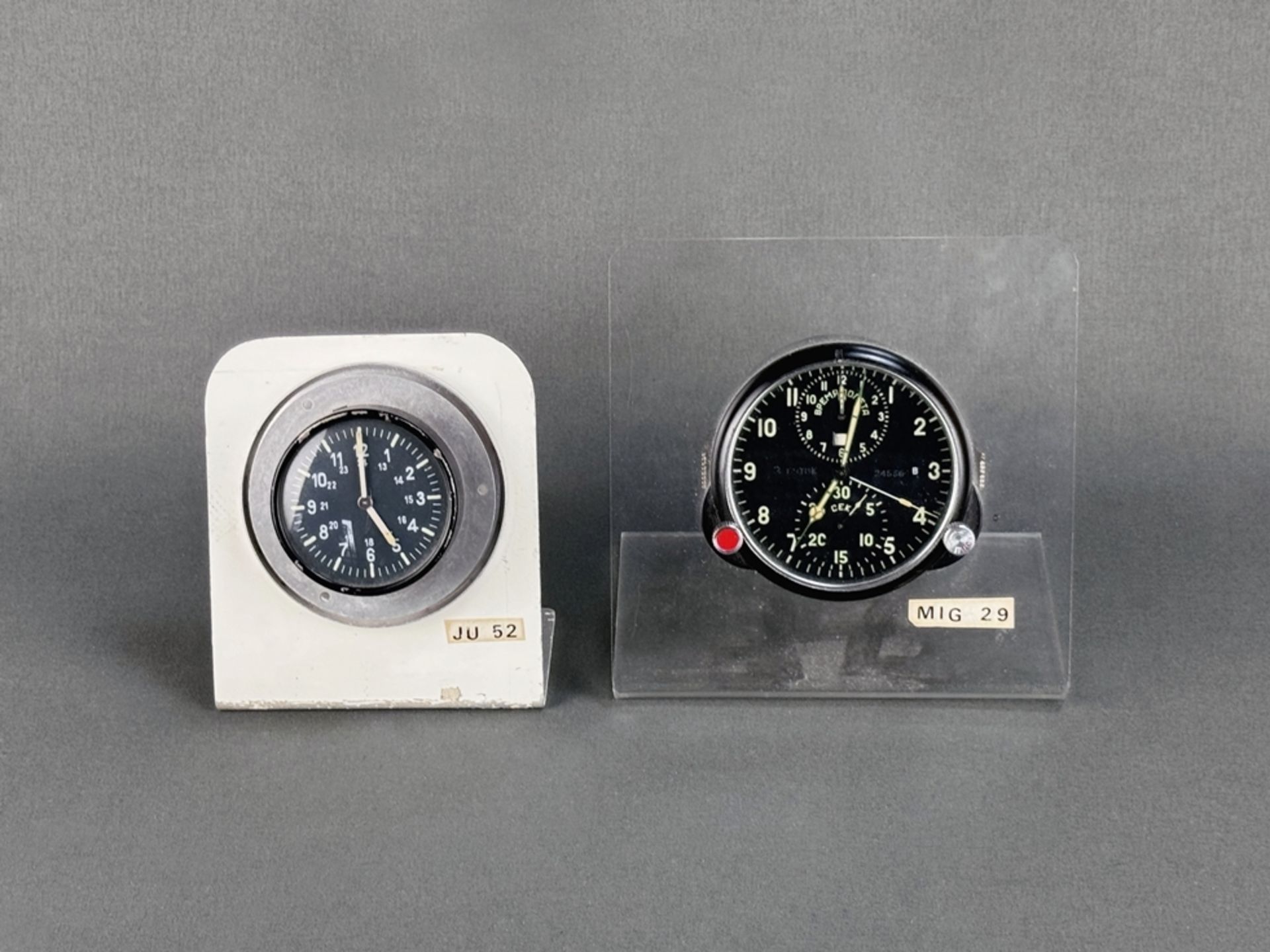 Two board clocks/airplane clocks, both start, one from a Mic 29, set in acrylic glass stand, dimens