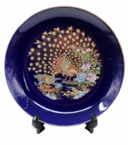 Round Japanese porcelain plate, decorated with a peacock pattern on a cobalt blue background.
