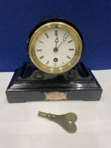 AN EBONISED CASED MANTLE CLOCK WITH 8 CM DIAL. HEIGHT 18CM AND KEY