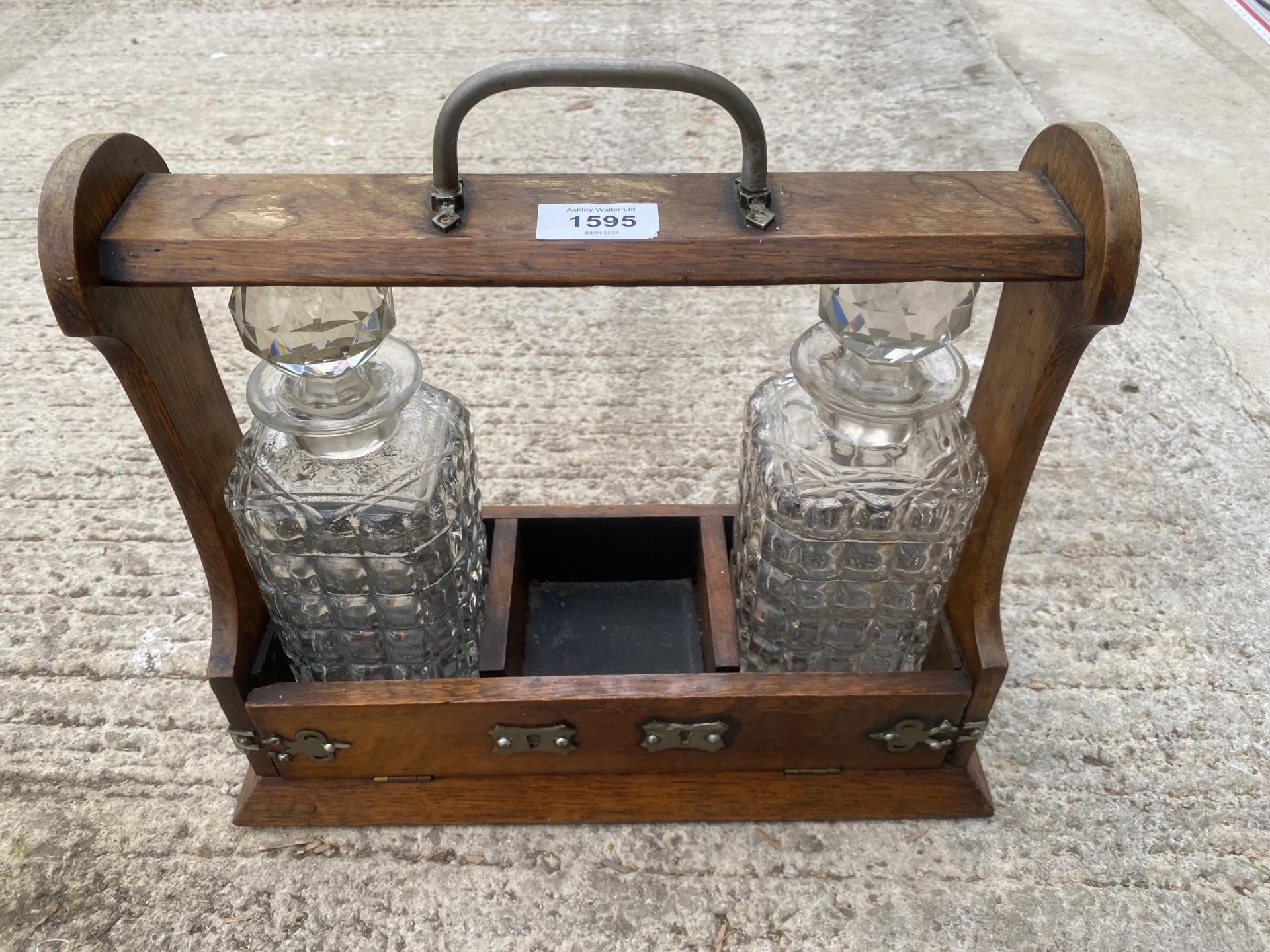 A VINTAGE OAK TANTALUS DECANTER HOLDER WITH TWO GLASS DECANTERS AND SILVER PLATE DETAIL