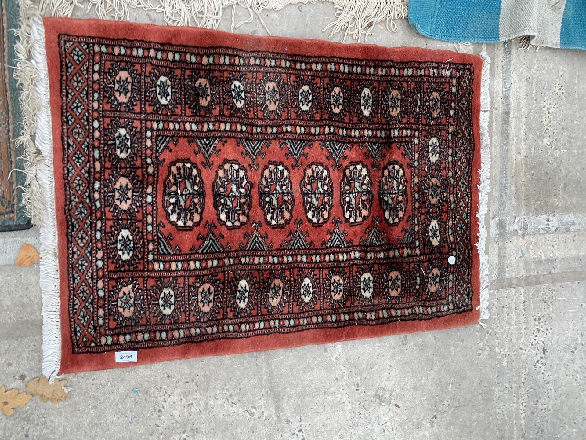 A SMALL RED PATTERNED FRINGED RUG