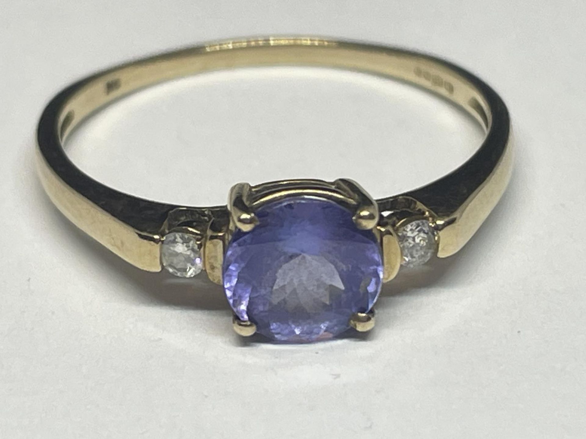 A 9 CARAT GOLD RING WITH A PURPLE GEMSTONE SURROUNDED BY TWO DIAMONDS SIZE R/S