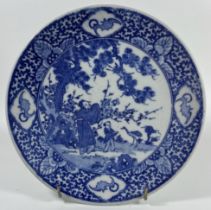 A JAPANESE BLUE AND WHITE POTTERY CHARGER PLATE WITH FIGURES IN GARDEN DESIGN, DIAMETER 22 CM