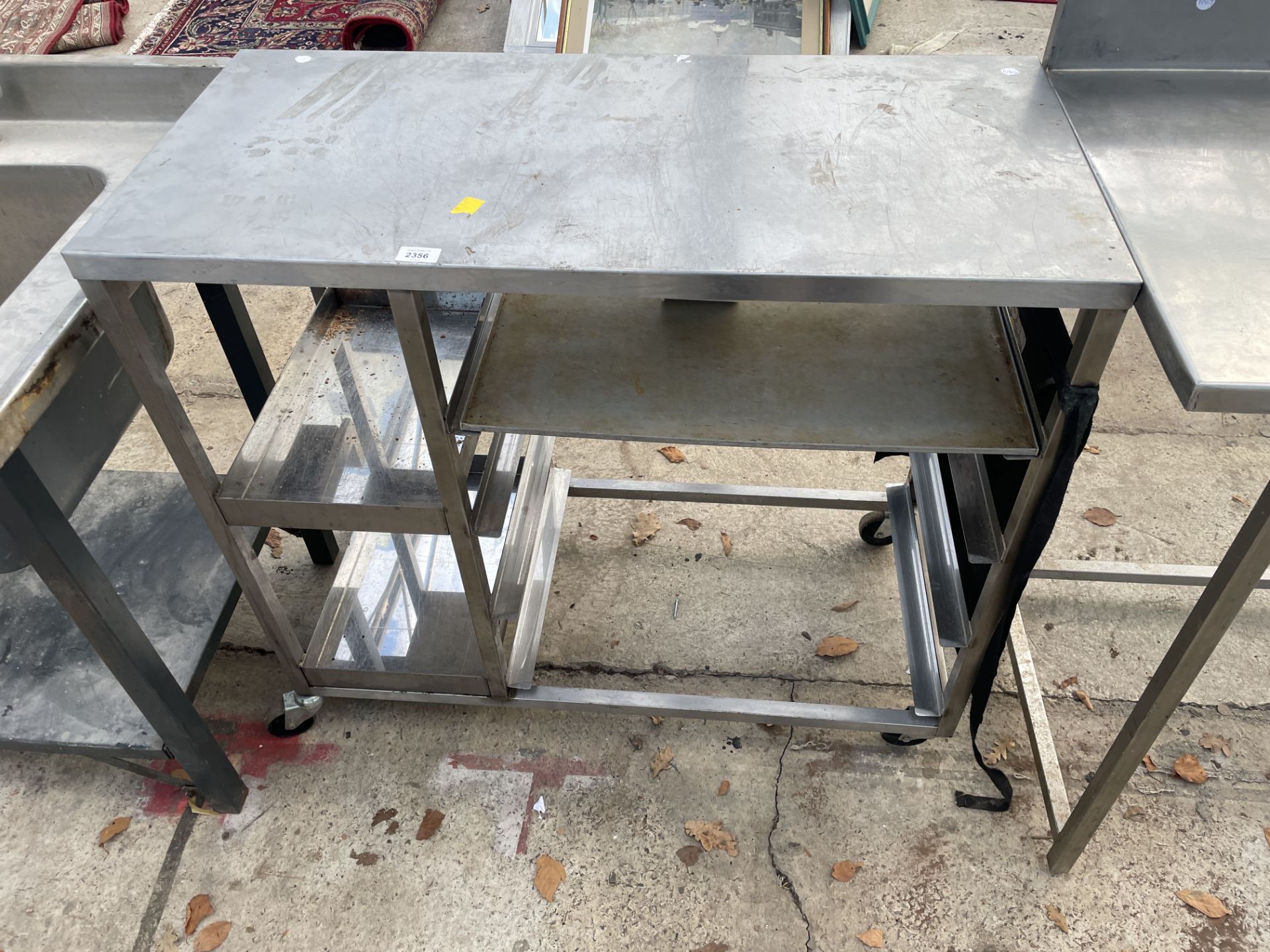 A SMALL STAINLESS STEEL FOUR WHEELED UNIT WITH TRAY STORAGE SECTIONS