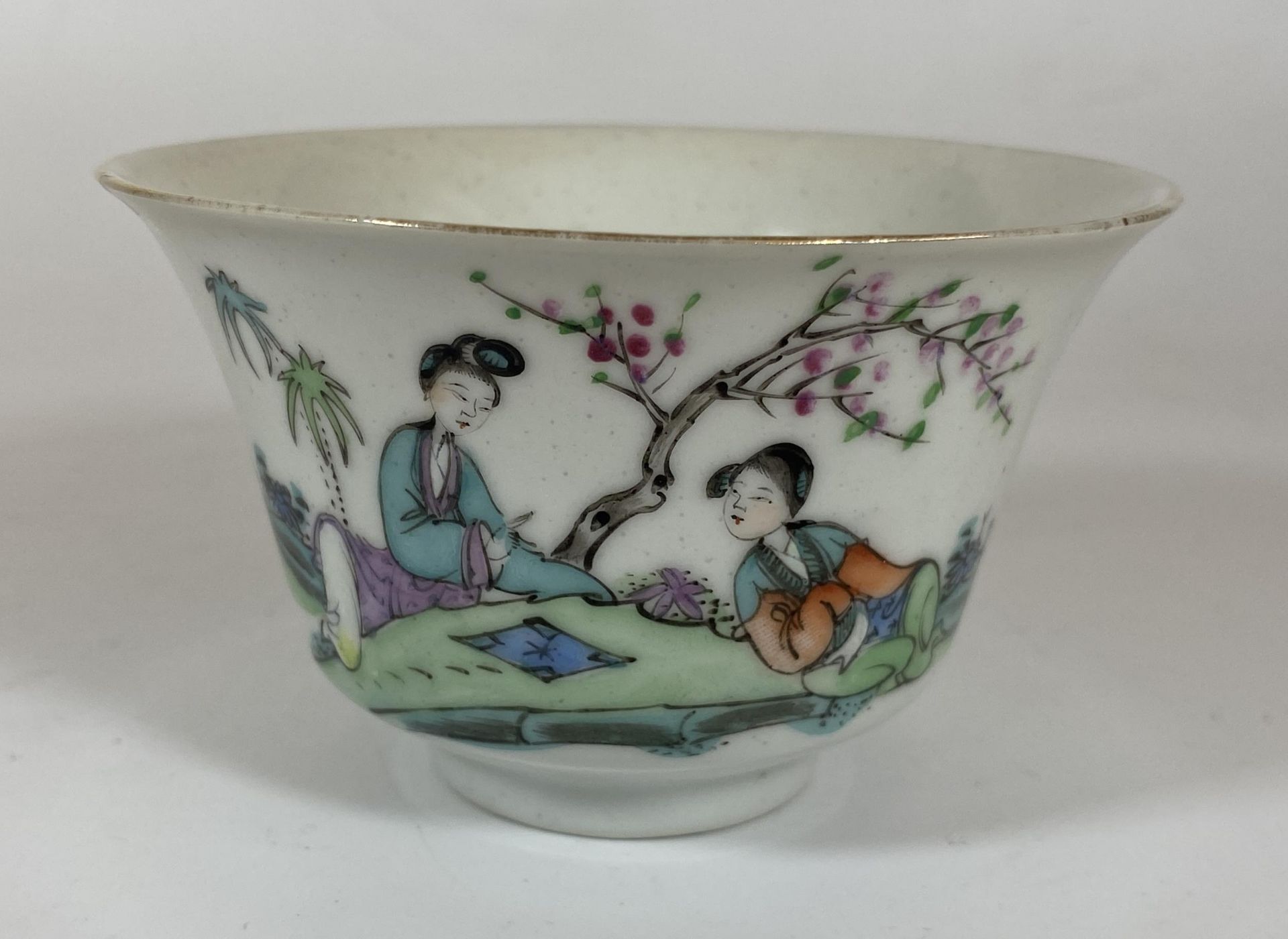 AN EARLY 20TH CENTURY CHINESE PORCELAIN TEA BOWL WITH FIGURES IN GARDEN DESIGN, FOUR CHARACTER