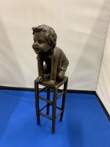 A BRONZE MODEL OF A CHILD KNEELING ON A STOOL SIGNED