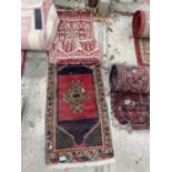 A SMALL RED PATTERNED FRINGED RUG AND A SMALL RED PATTERNED WALL HANGING