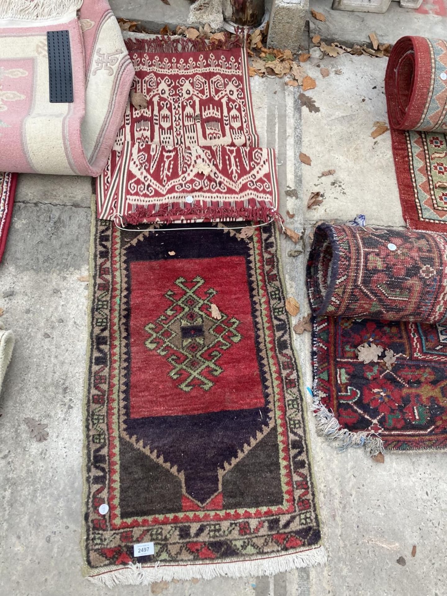 A SMALL RED PATTERNED FRINGED RUG AND A SMALL RED PATTERNED WALL HANGING