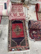 A SMALL RED PATTERNED FRINGED RUG AND A SMALL RED PATTERNED WALL HANGING