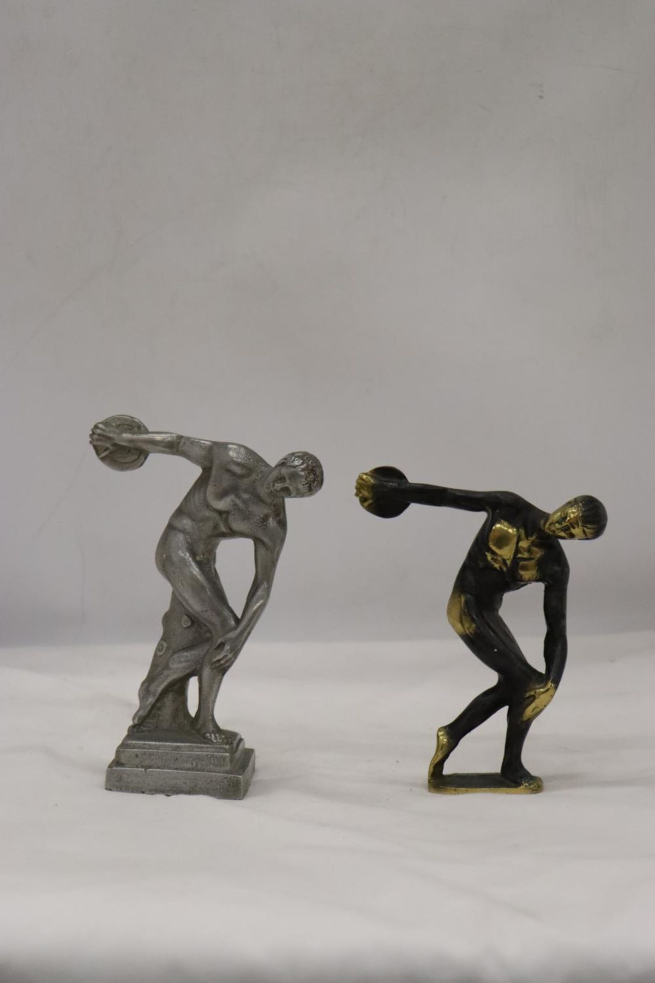 A HEAVY BRASS AND A WHITE METAL DISCUS THROWER