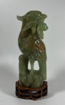 A CARVED JADE STYLE HARDSTONE MODEL OF A BIRD ON A CARVED WOODEN BASE, HEIGHT 20 CM