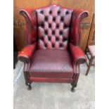 AN OXBLOOD WINGED FIRESIDE CHAIR ON CABRIOLE LEGS WITH BUTTON-BACK AND STUD DECORATION