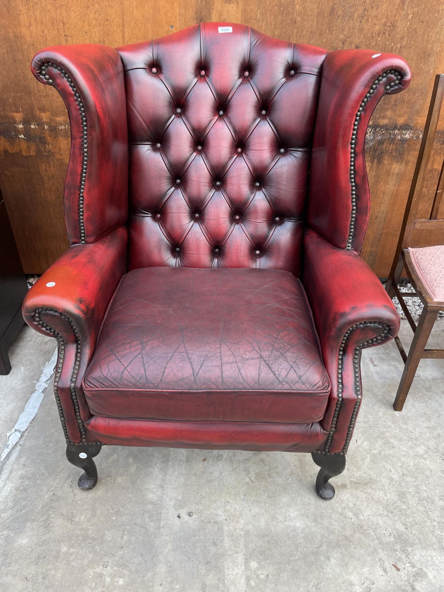 AN OXBLOOD WINGED FIRESIDE CHAIR ON CABRIOLE LEGS WITH BUTTON-BACK AND STUD DECORATION