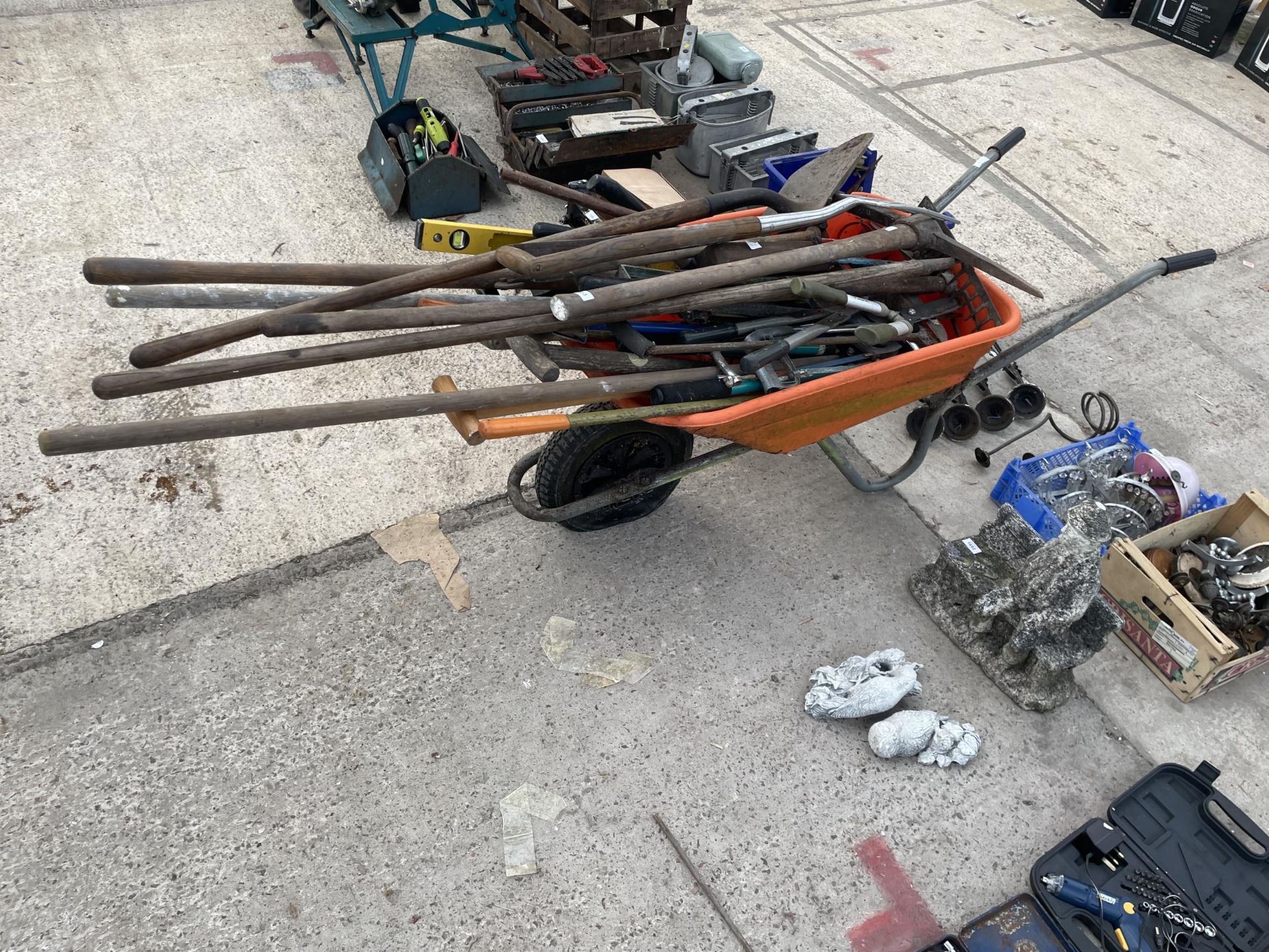 AN ORANGE PLASTIC WHEEL BARROW WITH A LARGE ASSORTMENT OF GARDEN TOOLS TO INCLUDE SPADES, FORKS