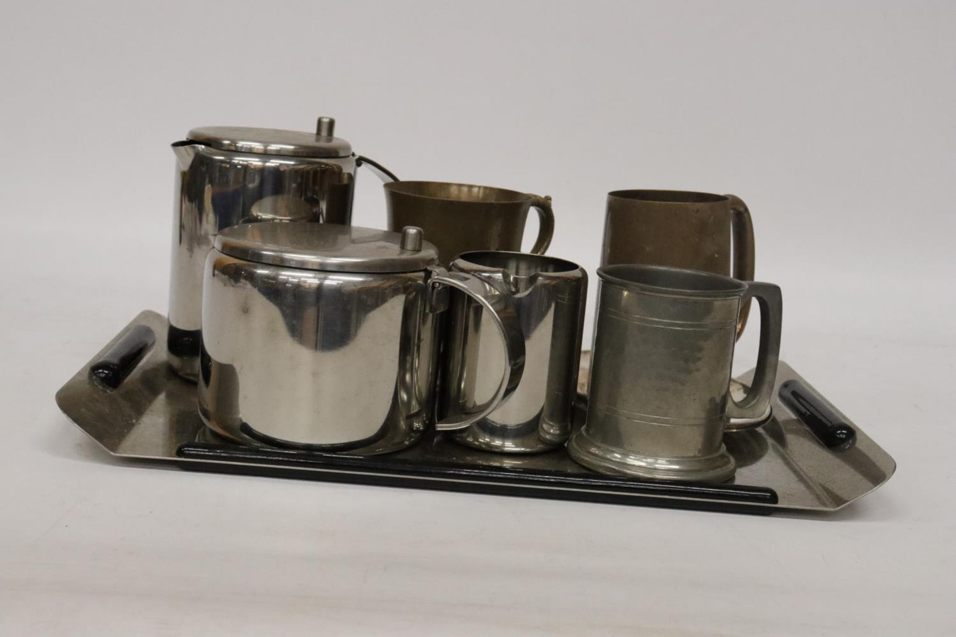 TWO BRASS TANKARDS, A PEWTER TANKARD, STAINLESS STEEL TEA POT, HOT WATER JUG AND CREAM JUG ON A TRAY