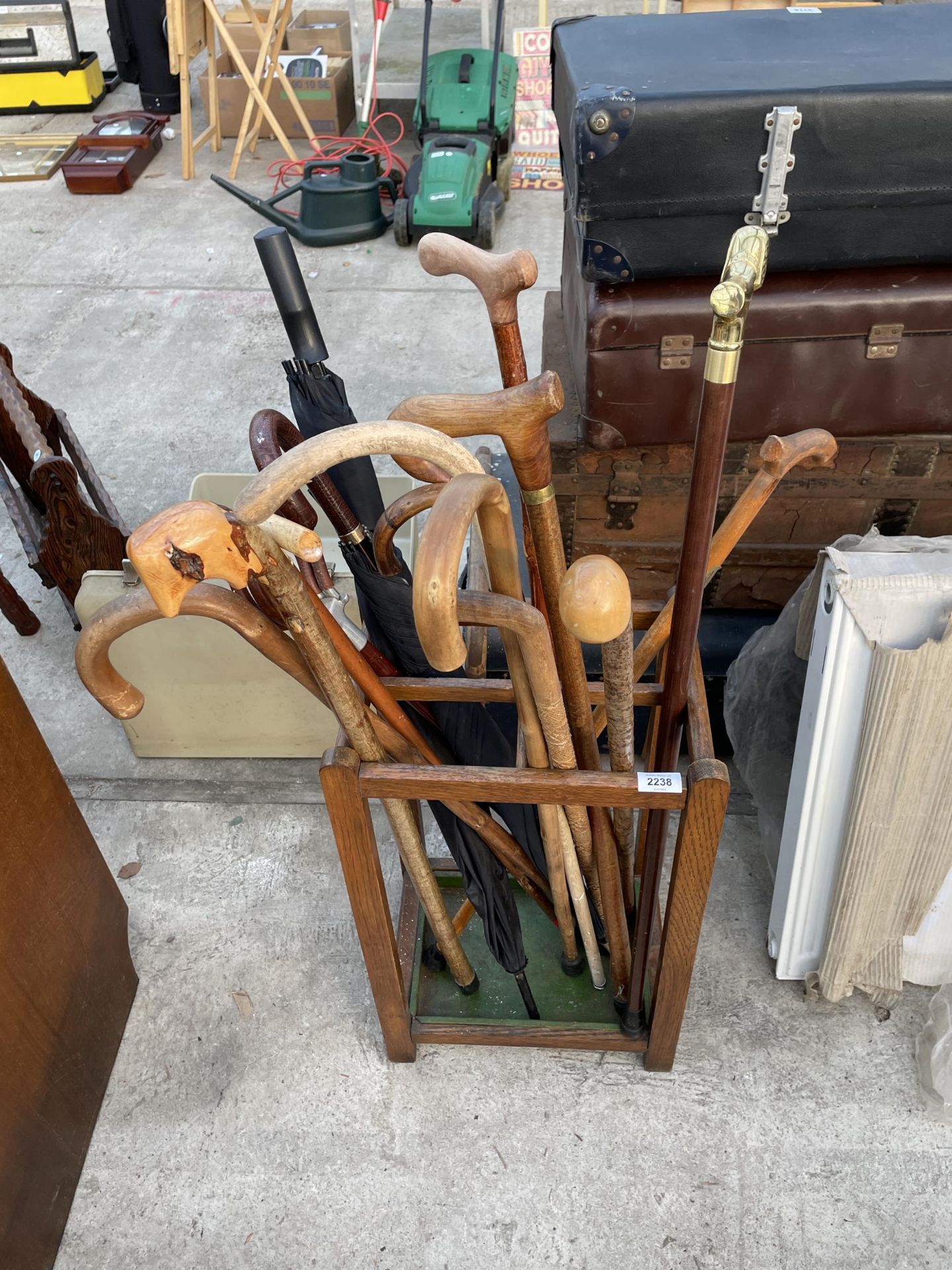 AN OAK STICK STAND WITH AN ASSORTMENT OF UMBRELLAS AND WALKING STICKS TO INCLUDE ONE WITH A SILVER