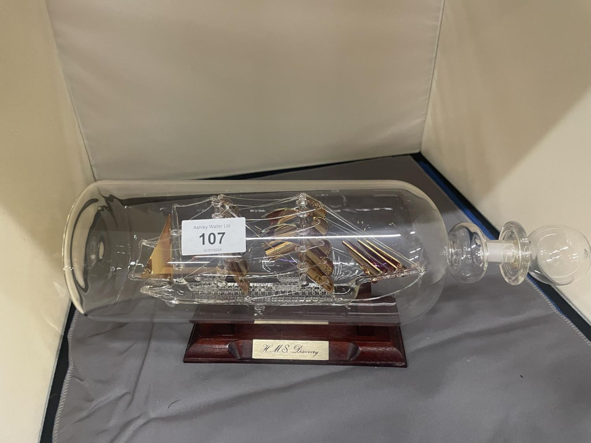 A SHIP IN A BOTTLE 'HMS DISCOVERY' ON A WOODEN STAND, HEIGHT 15CM, LENGTH 34CM