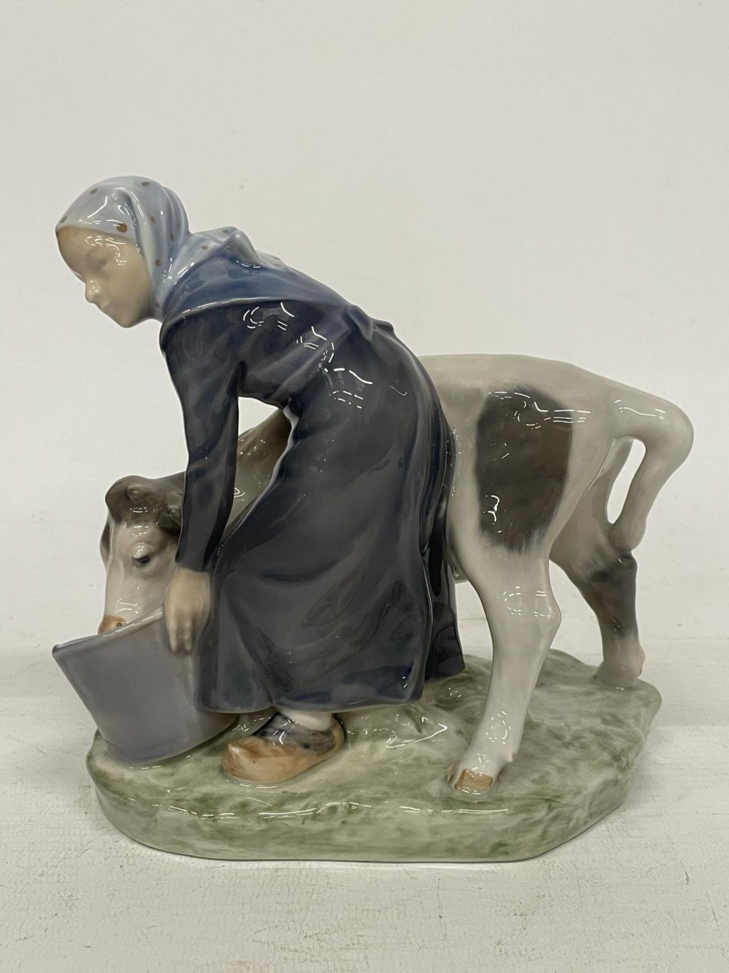 A ROYAL COPENHAGEN FIGURE OF A FARMGIRL AND CALF - DECORATION NUMBER 779 - DESIGNED BY CHRISTIAN