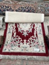 A SMALL RED PATTERNED FRINGED RUG