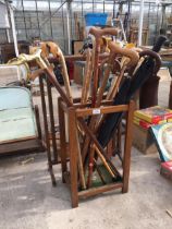 AN OAK STICK STAND WITH AN ASSORTMENT OF UMBRELLAS AND WALKING STICKS TO INCLUDE ONE WITH A SILVER