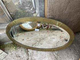 AN OVAL MIRROR WITH EMBOSSED BRASS FRAME