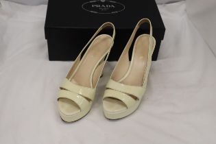 A PAIR OF CREAM HIGH HEELED SHOES, MARKED WITH A GOLD COLOURED 'PRADA' TO THE UNDERSIDE, IN A BOX