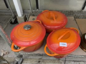 THREE LARGE ORANGE COOKING PANS IN THE STYLE OF LE CREUSET