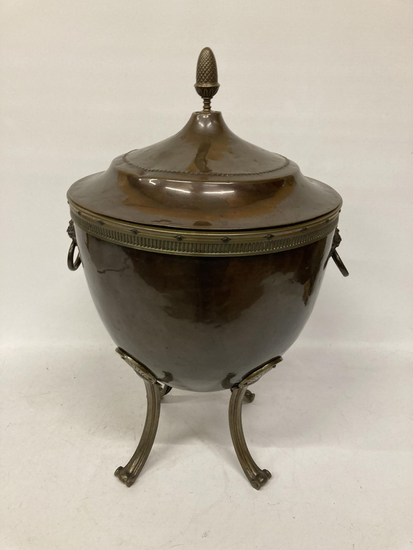 A BRASS AND COPPER COAL BOX ON FOUR LEGS, WITH LION HEAD HANDLES, AN ACORN TOP AND LINER