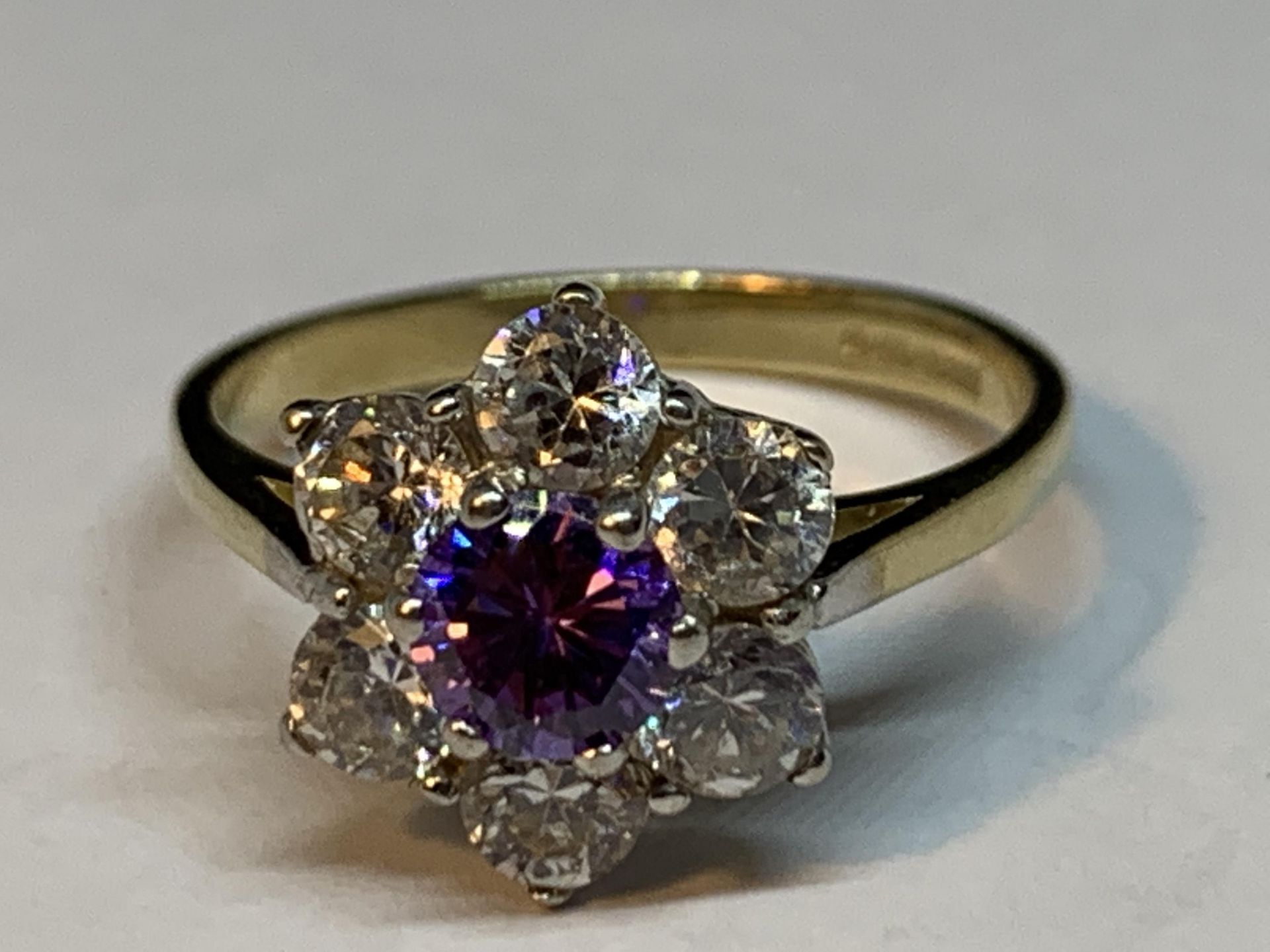 A 9 CARAT GOLD RING WITH CENTRE AMETHYST SURROUNDED BY CUBIC ZIRCONIAS IN A FLOWER DESIGN SIZE P/Q