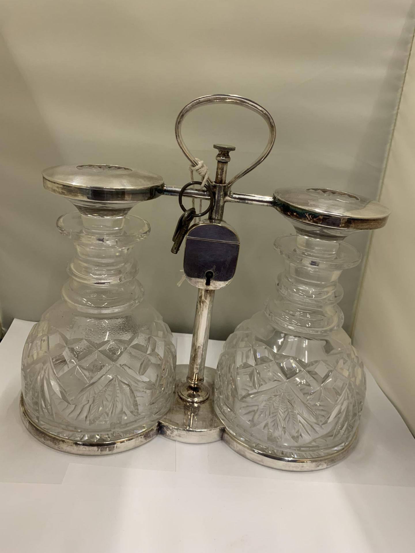 A WHITE METAL TANTALUS WITH TWO CUT GLASS DECANTERS WITH PADLOCK AND KEY