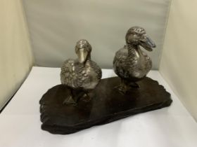 A VINTAGE PAIR OF WHITE METAL DUCKS ON A WOODEN PLINTH