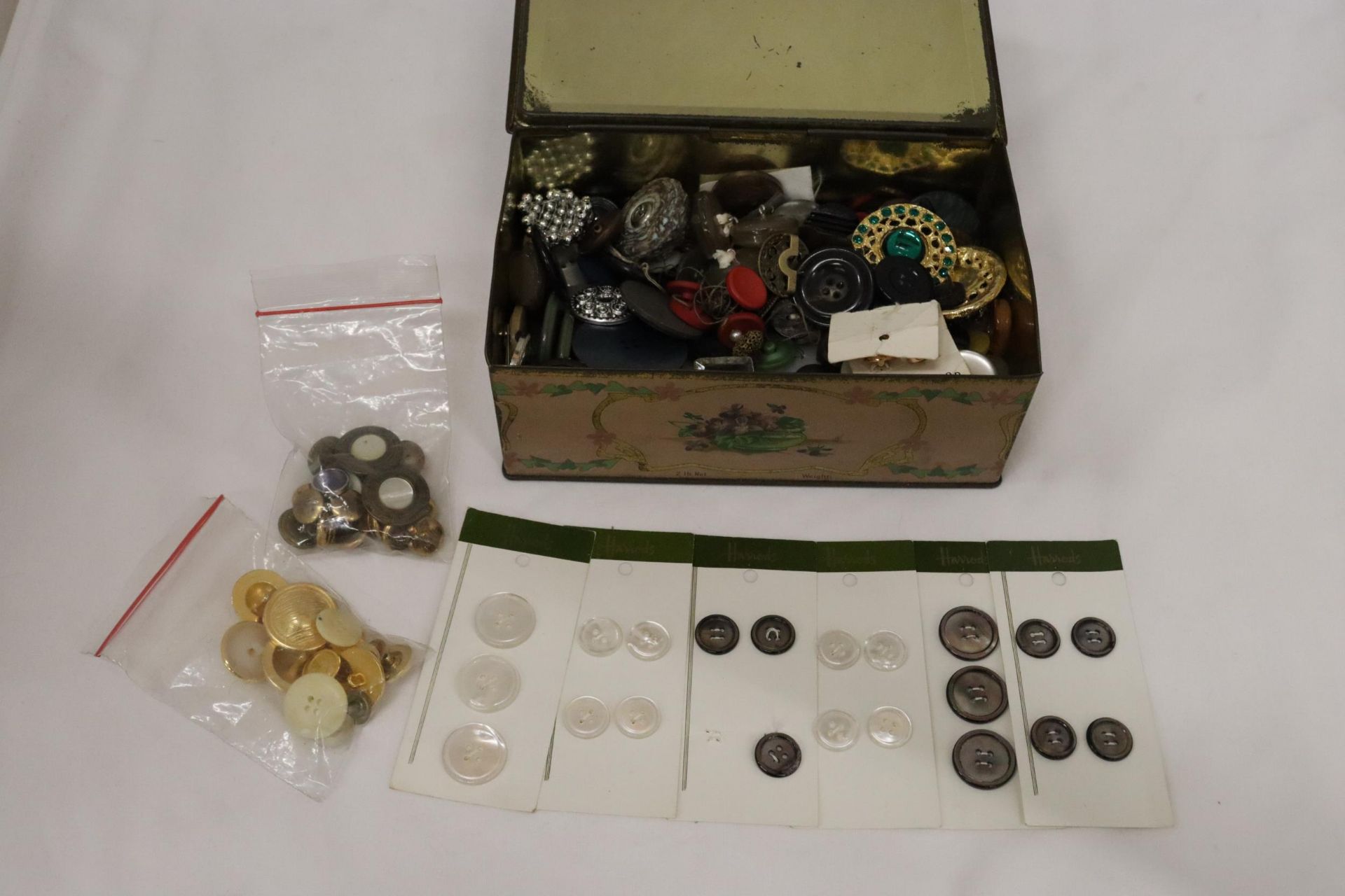 A VINTAGE TIN CONTAINING A LARGE QUANTITY OF VINTAGE BUTTONS TO INCLUDE VOGUE STAR, HARRODS, ETC.,