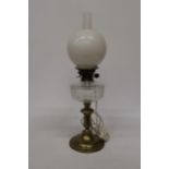 A 19TH CENTURY OIL LAMP CONVERTED TO ELECTRIC WITH A BRASS BASE, CLEAR CUT GLASS RESERVOIR, MILK