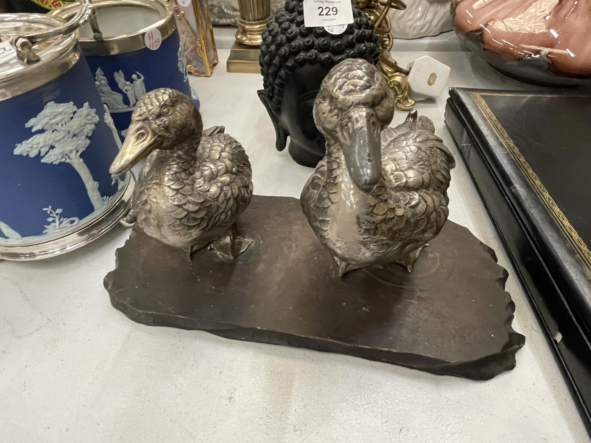 A VINTAGE PAIR OF WHITE METAL DUCKS ON A WOODEN PLINTH