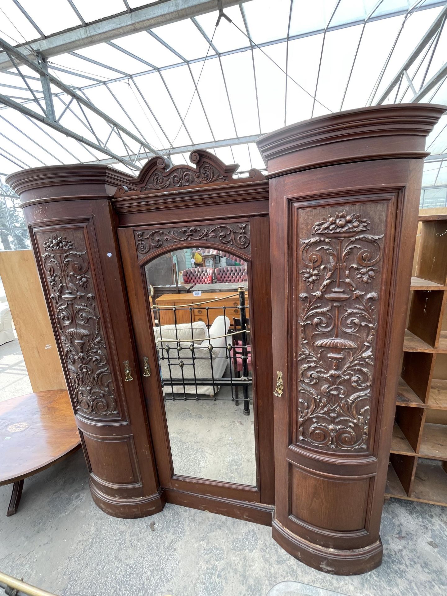 A VICTORIAN MAHOGANY DOUBLE BOW FRONTED MIRROR DOOR WARDROBE WITH FOLIATE CARVED PANELS AND THREE