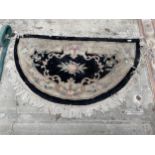 A BLACK PATTERNED HALF MOON FRINGED RUG