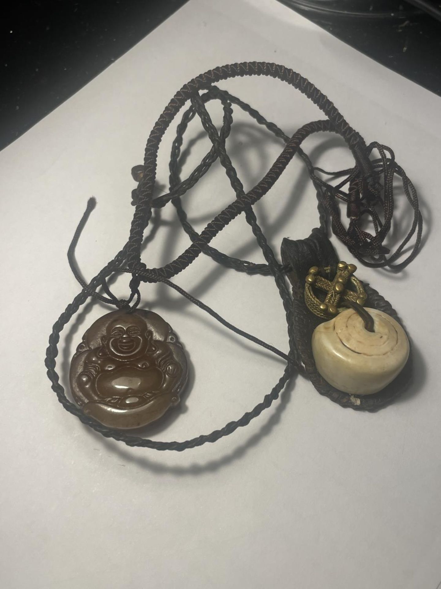 TWO NECKLACES TO INCLUDE A CARVED BUDDHA PENDANT AND A TALISMAN GOOD LUCK AMULET BOTH ON A LEATHER