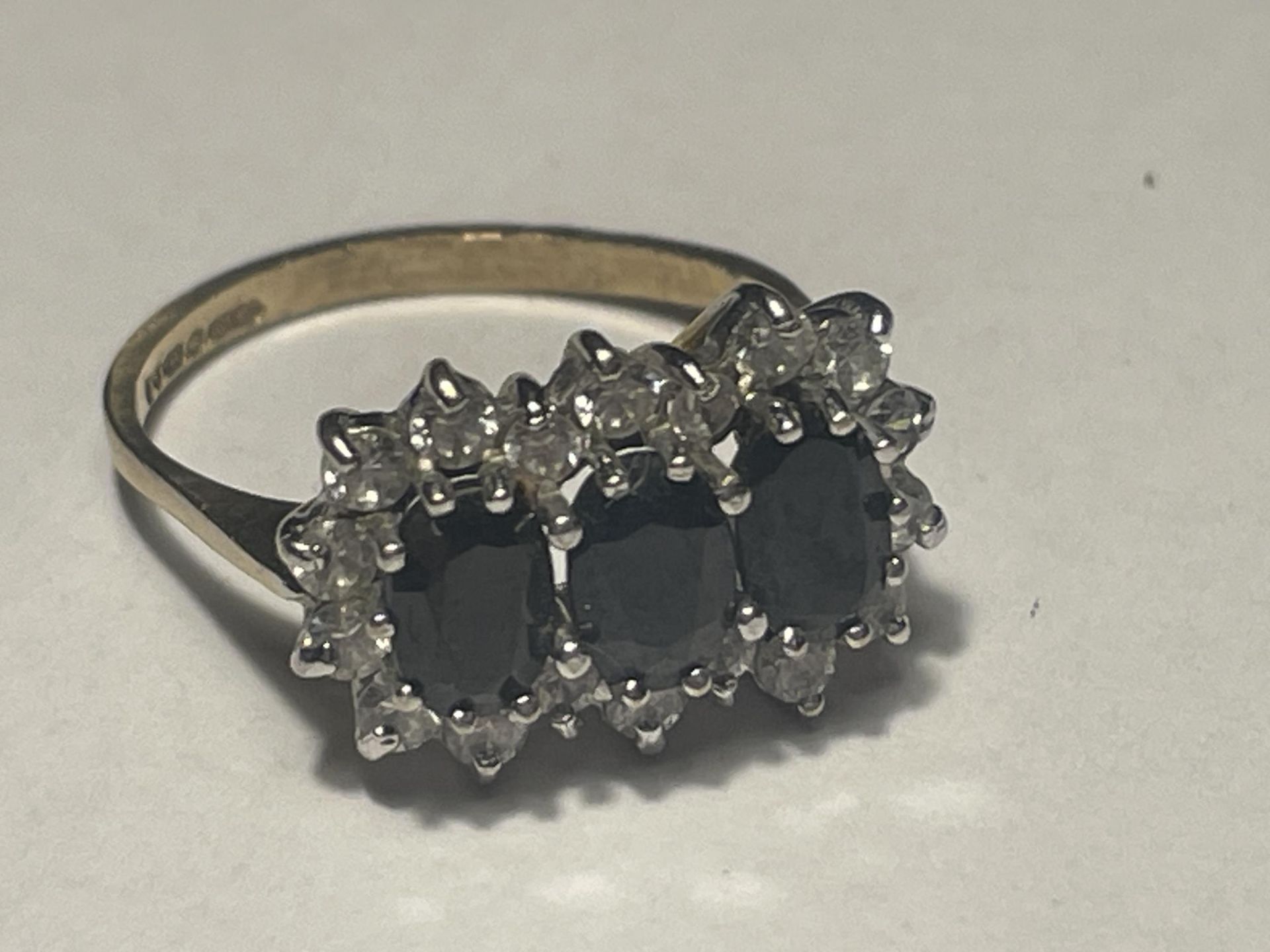 A 9 CARAT GOLD RING WITH THREE LARGE IN LINE SAPPHIRES SURROUNDED BY CUBIC ZIRCONIAS SIZE L/M