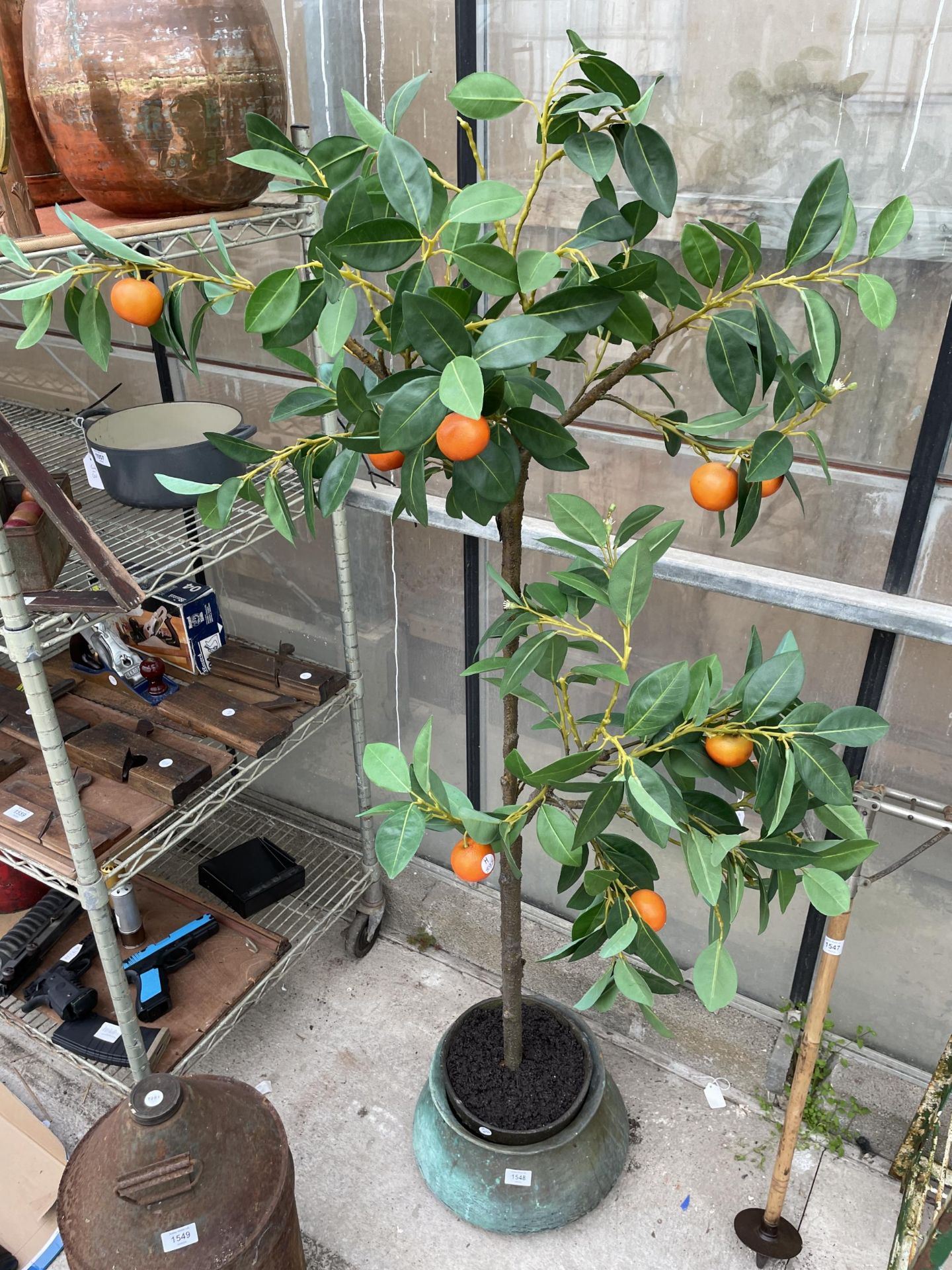 AN ARTIFICIAL ORANGE TREE WITH A DECORATIVE BRASS PLANTER