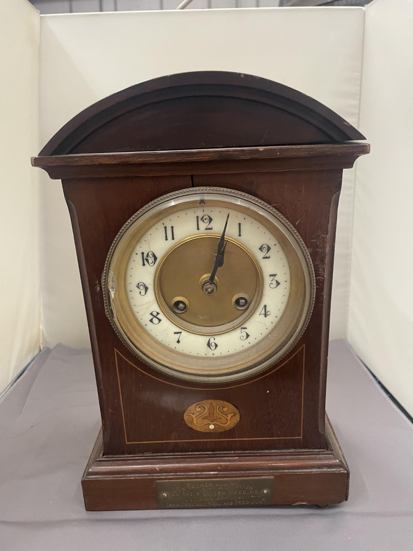 A MAHOGANY INLAID MANTLE CLOCK WITH INSCRIPTION PLATE (A/F LEG MISSING)