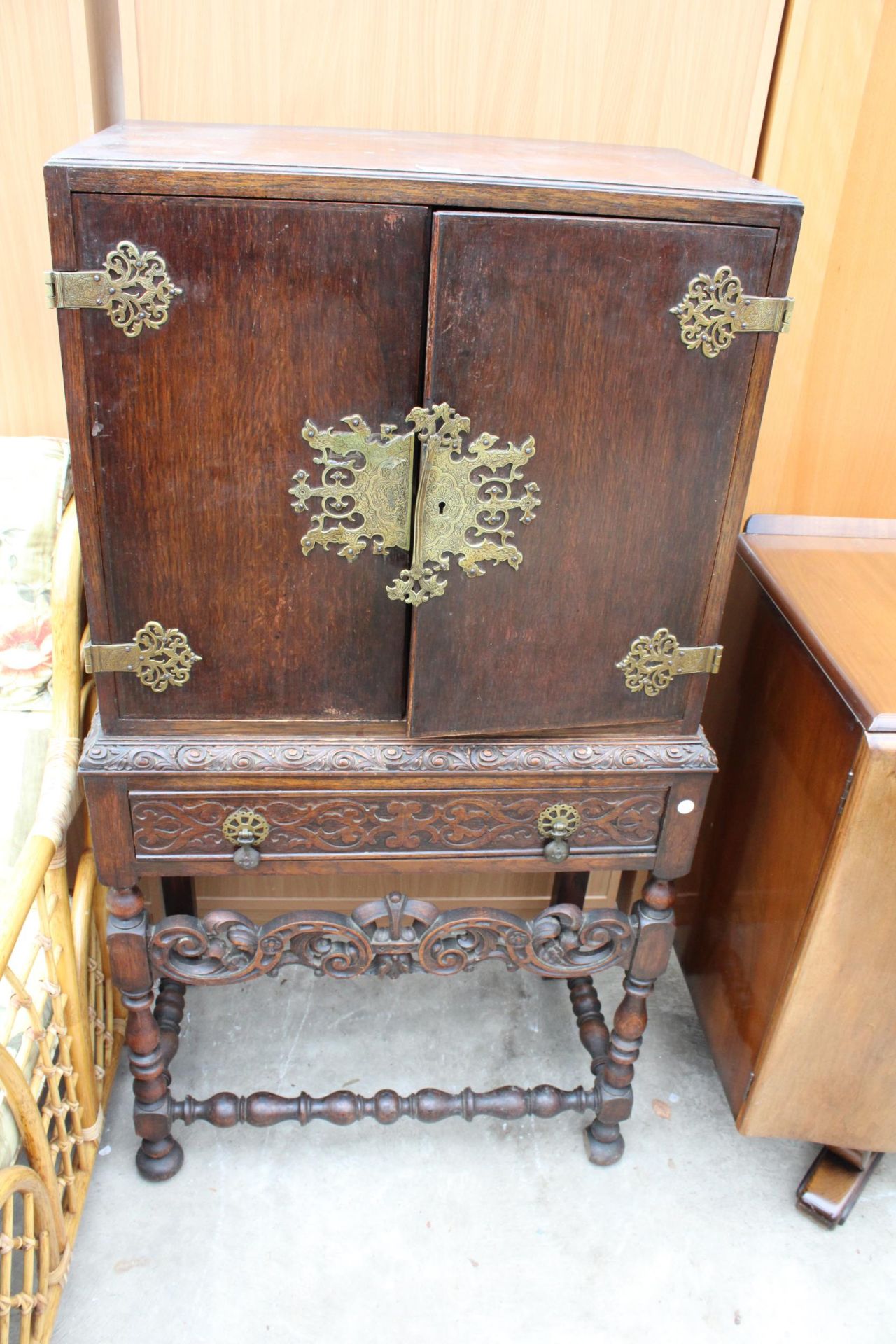 AN EARLY 20TH CENTURY OAK JACOBEAN STYLE COCKTAIL CABINET ENCLOSING SLIDES AND A SINGLE DRAWER ON