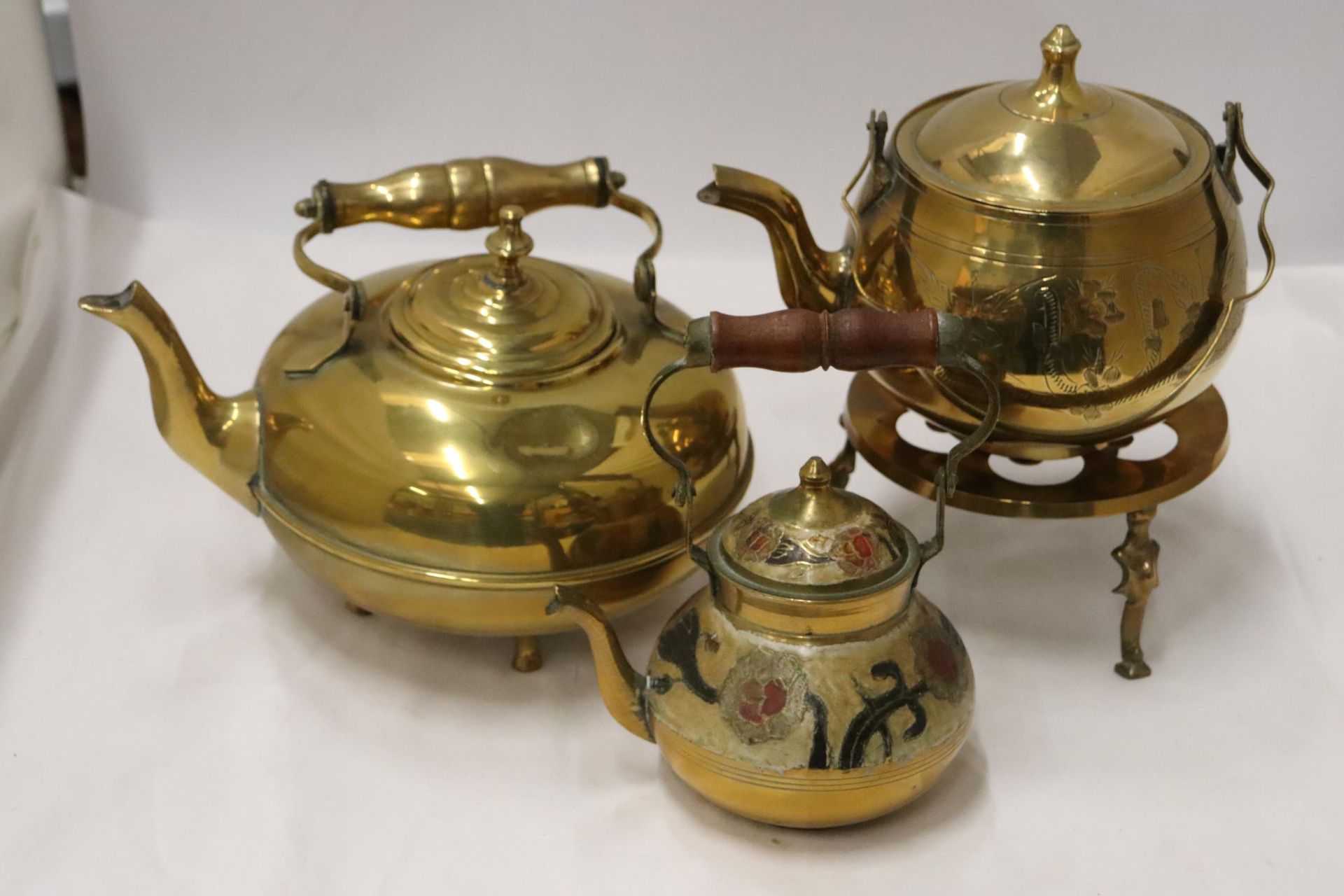 TWO BRASS KETTLES, A CLOISONNE KETTLE AND A TRIVET