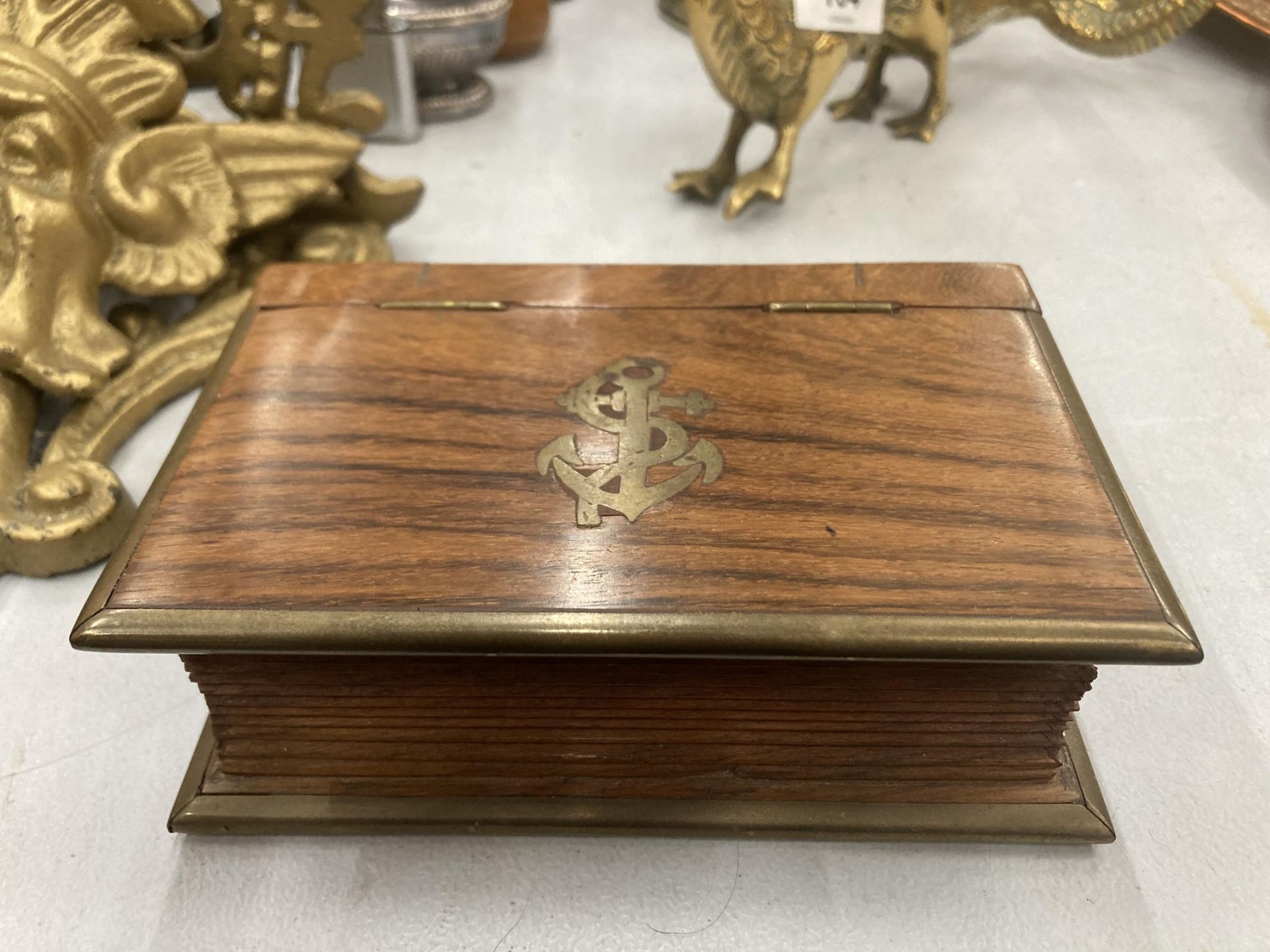 A MAHOGANY BOX IN THE SHAPE OF A BOOK WITH BRASS EDGES AND AN ANCHOR MOTIF TO THE LID