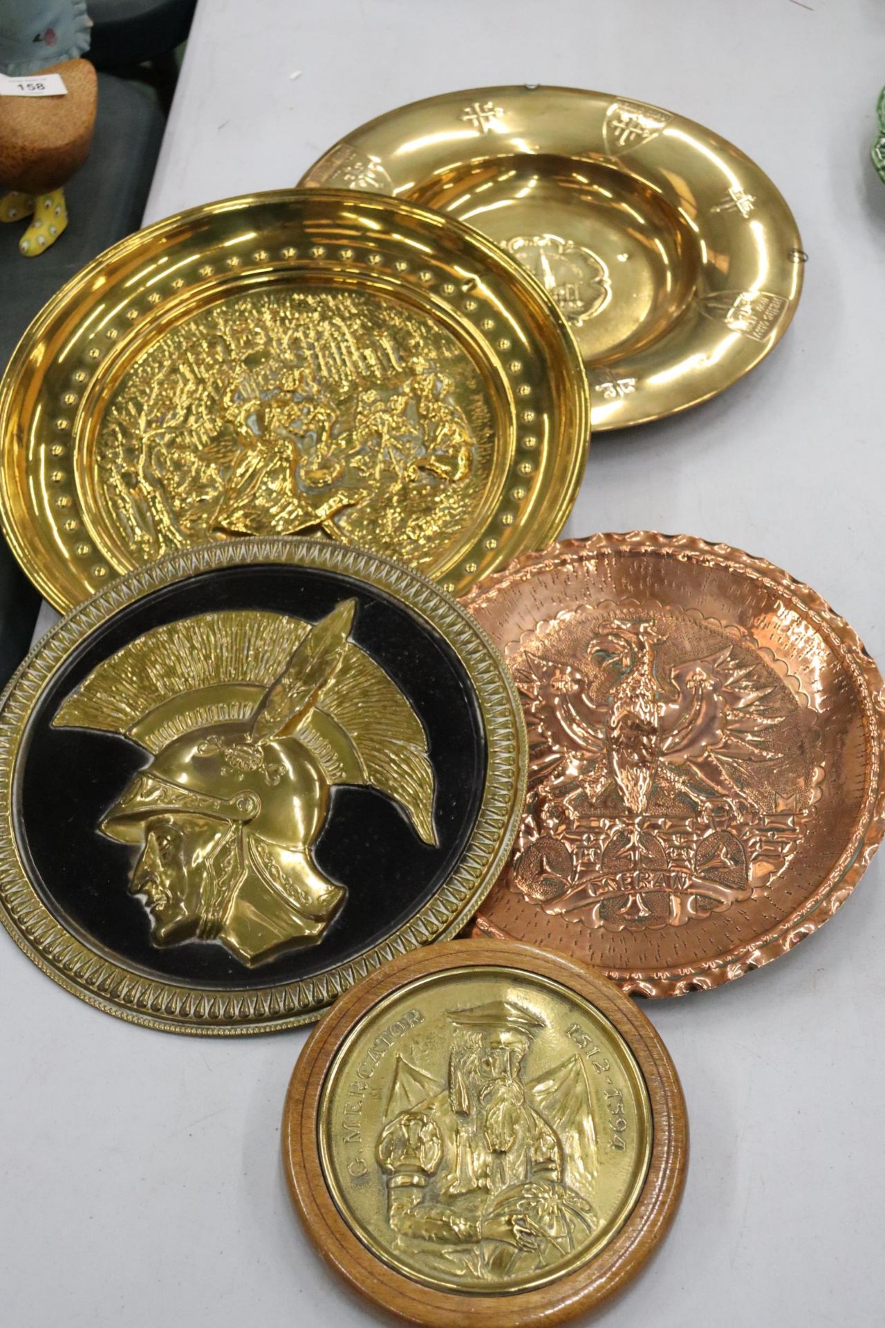 FIVE BRASS AND COPPER PLATES TO INCLUDE A HAMMERED BRASS GREEK WALL PLATE, COAT OF ARMS, ETC.,