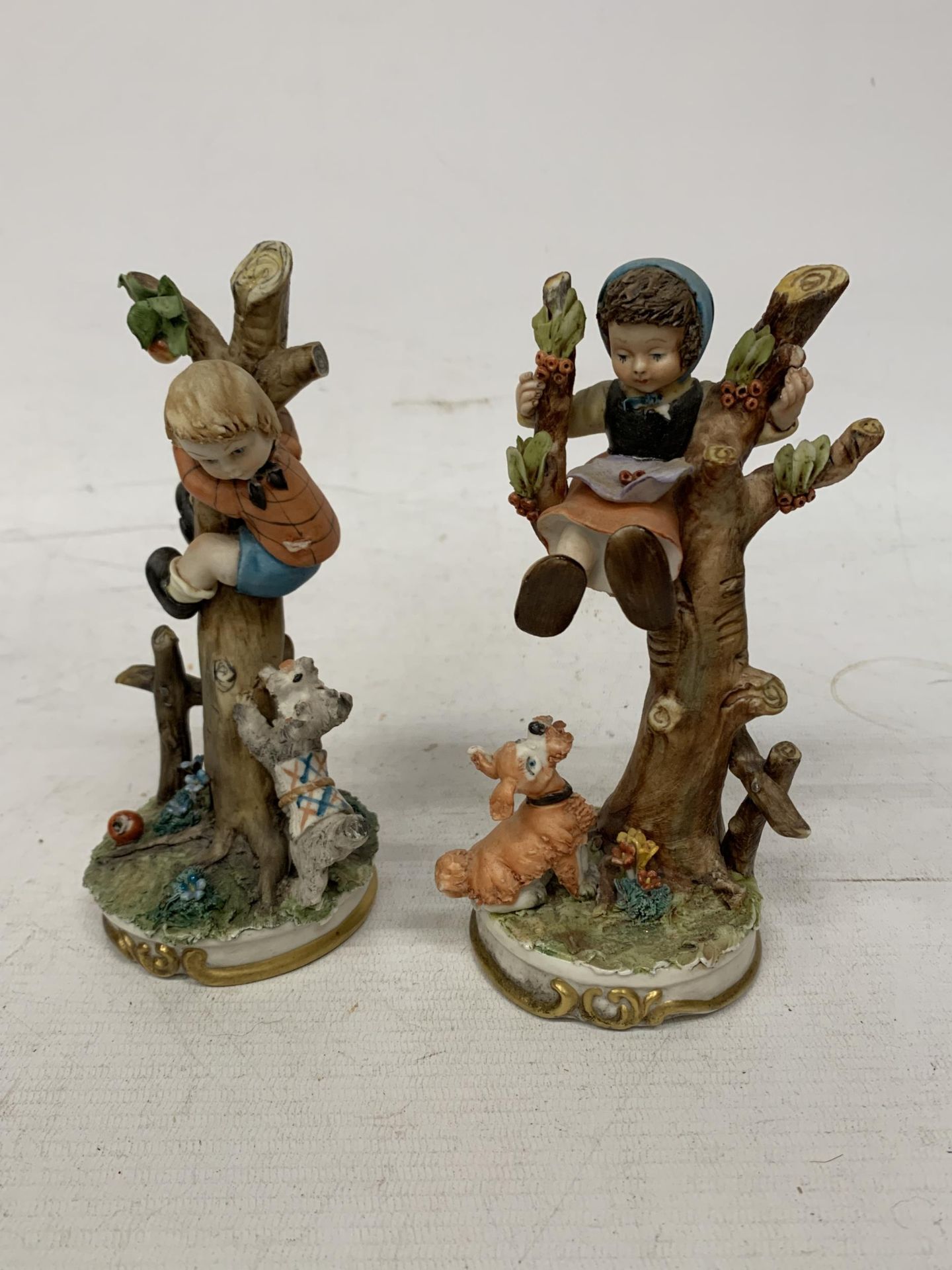 TWO CAPODIAMONTE FIGURES OF A GIRL AND A BOY IN A TREE WITH A DOG BARKING BELOW